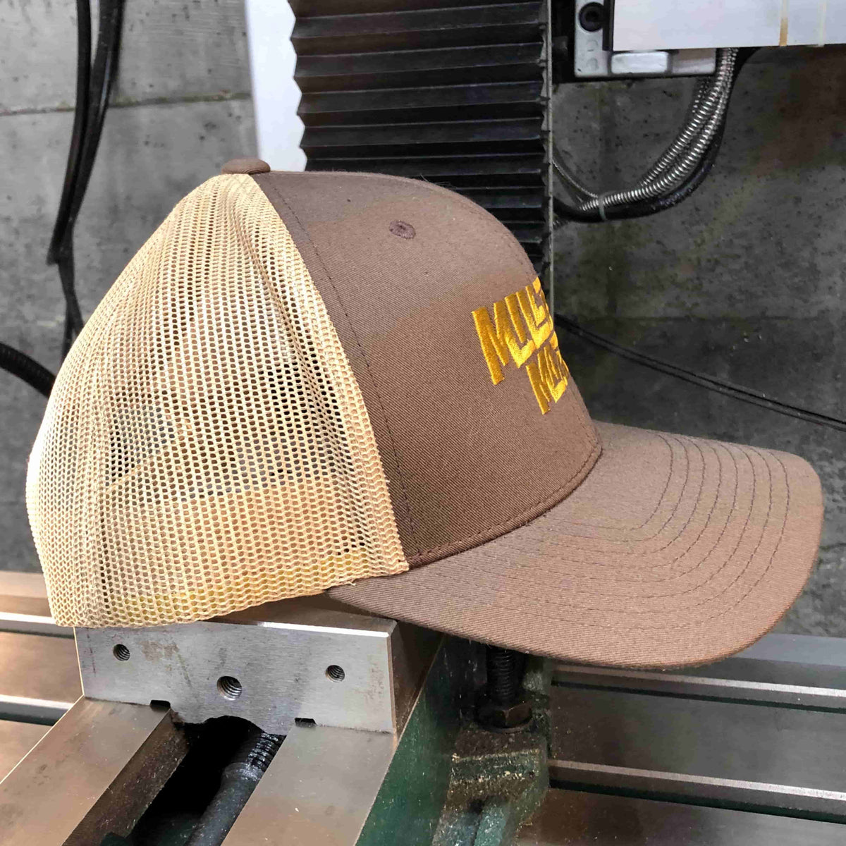 Side photo of Miller Machine Trucker Cap in brown, with gold embroidery.