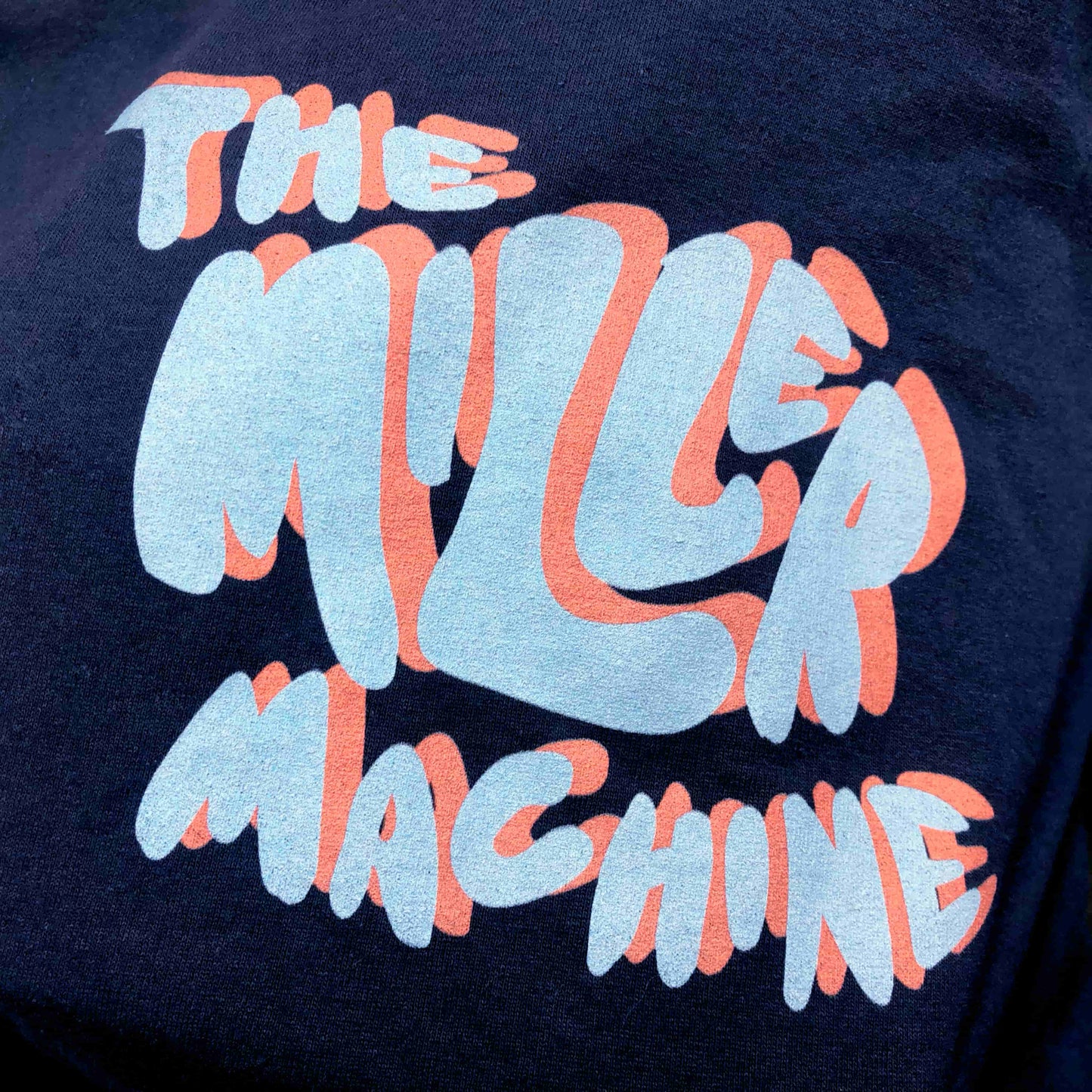 Closeup photo of the Faux 3D text on "The Miller Machine" long-sleeved t-shirt in color Navy.