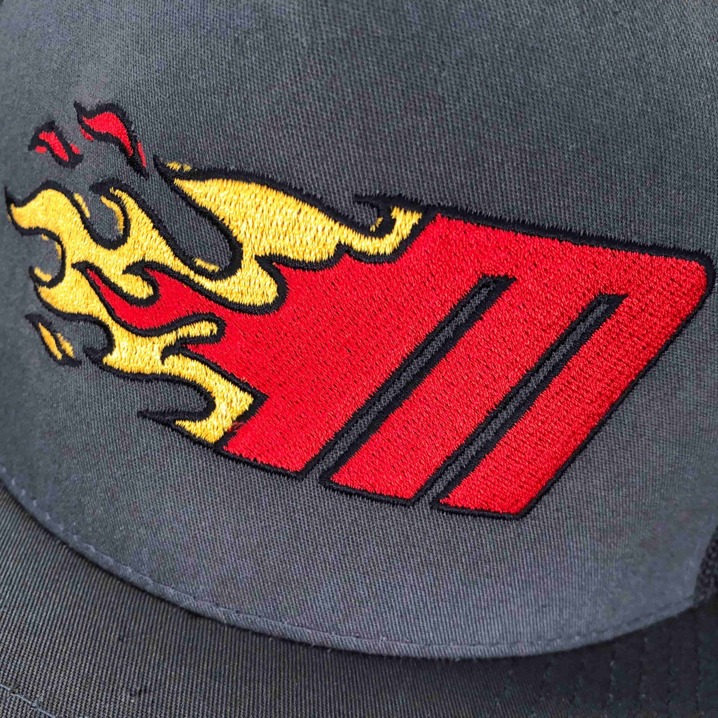 Close up photo of Miller Machine 5 panel trucker cap with a Flaming M in red and yellow. Cap is a grey color.